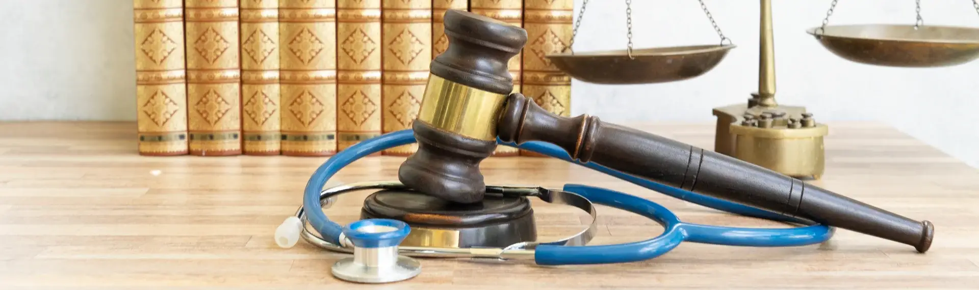 Picture of a gavel with a stethoscope with books and scale in the background.